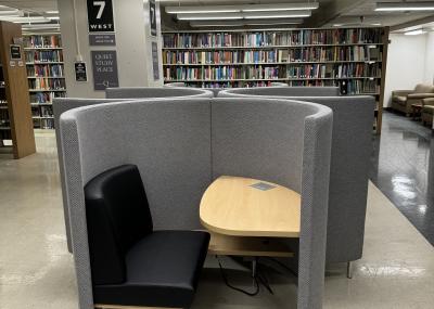 Semi-enclosed study pod with a cushioned seat and wooden desk, with a built-in electrical outlet