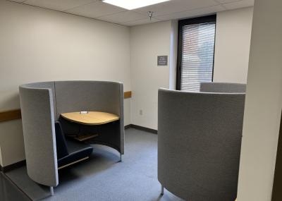 Two semi-enclosed study pods next to a window. Each study pod has a cushioned chair and a desk with a built-in electrical outlet.